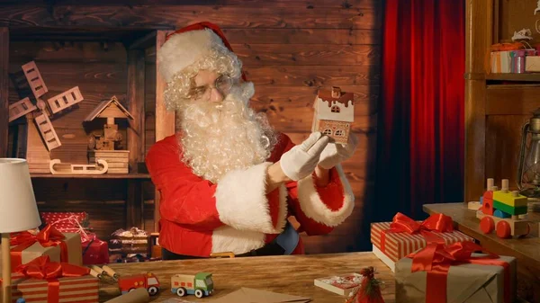 Kerstman Aan Tafel Houdt Een Houten Speelgoed Zijn Handen Bij — Stockfoto