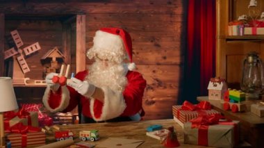 Noel Baba hediyelerle masada ve evinde tahta bir oyuncak yapıyor.
