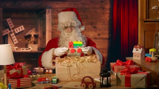 Άγιος Βασίλης Στο Τραπέζι Κρατά Ένα Ξύλινο Παιχνίδι Στα Χέρια — Αρχείο Βίντεο