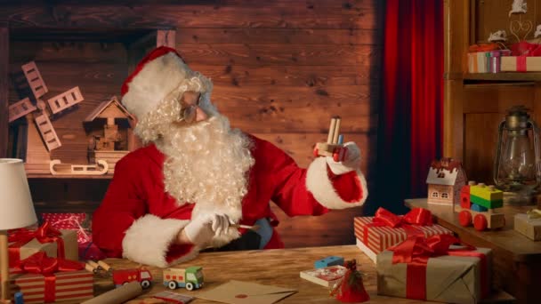 Jultomten Vid Bordet Med Presenter Och Målar Träleksak Vid Sitt — Stockvideo