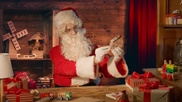 Jultomten Vid Bordet Håller Träleksak Sina Händer Vid Sitt Hus — Stockvideo