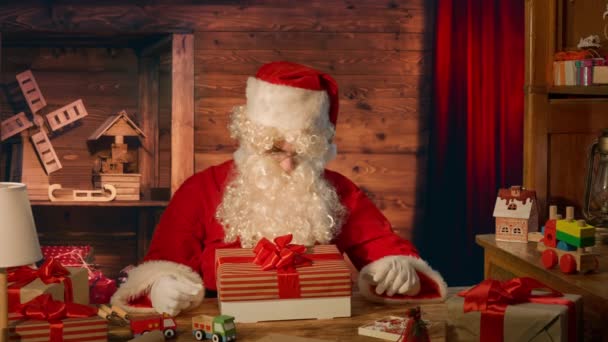 Kerstman Aan Tafel Met Geschenken Kijken Naar Een Doos Met — Stockvideo