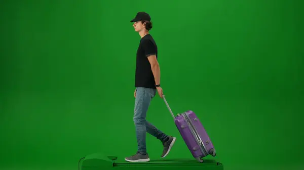 Airport creative advertisement concept. Portrait of person tourist isolated on chroma key green screen background. Young man in cap with suitcase walking and looking around.