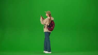 Uçak kreatif havaalanı reklam konseptiyle seyahat etmek. Krom anahtar yeşil ekran arka planında izole edilmiş gezgin portresi. Sırt çantalı genç kız kalkış panosunu ve akıllı telefonu kontrol ediyor..