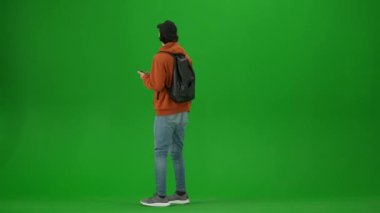 Uçak kreatif havaalanı reklam konseptiyle seyahat etmek. Krom anahtar yeşil ekran arka planında izole edilmiş gezgin portresi. Sırt çantalı genç adam kalkış panosunu ve akıllı telefonu kontrol ediyor..