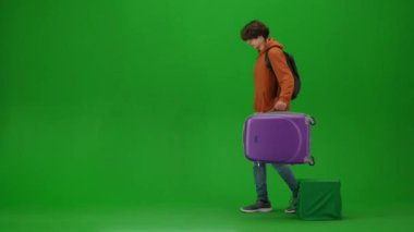 Uçak kreatif havaalanı reklam konseptiyle seyahat etmek. Krom anahtar yeşil ekran arka planında izole edilmiş gezgin portresi. Genç adam yere ağır bir bavul koyar, tutucu çeker gider..