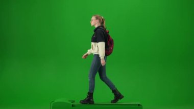 Uçak kreatif havaalanı reklam konseptiyle seyahat etmek. Krom anahtar yeşil ekran arka planında izole edilmiş gezgin portresi. Sırt çantalı, gözlüklü genç kız yürüyor ve etrafa bakıyor..