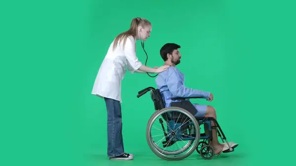 医疗病房和康复创意的色彩关键绿色屏幕概念 穿着长袍坐在轮椅上的成年男性病人 带听诊器的女护士 检查他的肺在后面呼吸 — 图库照片