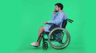 Tıp koğuşu ve sağlık rehabilitasyon reklam konsepti. Tekerlekli sandalyedeki adam akıllı telefon tutuyor ve konuşuyor, gülümsüyor. Krom anahtar yeşil ekranda izole edildi.