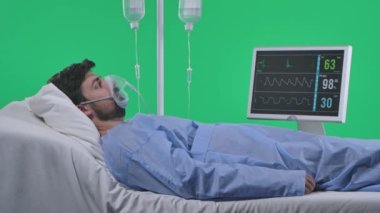 Tıp koğuşu ve sağlık rehabilitasyon reklam konsepti. Serumla, nefes maskesiyle ve monitörle yatakta bir adam var. Adam şok olmuş bir ifadeyle nefes alıyor. Krom anahtar yeşil ekranda izole edildi.