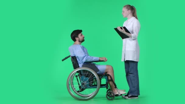 医療区 医療リハビリテーション広告コンセプト 車椅子の男は看護師と話し 質問に答え クリップボードを書く女性は空白を書いています クロマキーグリーンスクリーンに分離 — ストック動画