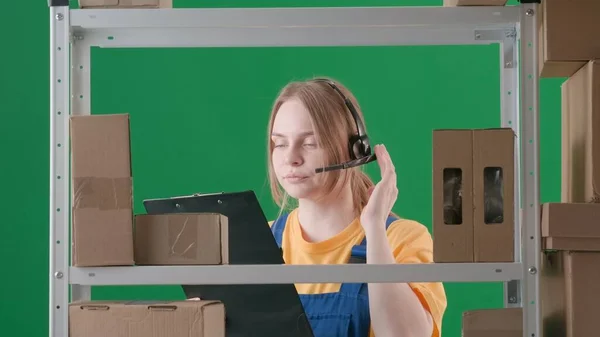 框架在绿色的背景上 铬钥匙 描述了一个穿着制服和耳机的年轻女人 演示一个工人 仓库的仓库管理员 她拿着一块石板 看着什么东西 — 图库照片