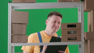 Yeşil arka planda çerçevelenmiş, kromakey. İş üniformalı bir adamı gösteriyor. Depoda bir depocuyu gösteriyor. Depoya kutu saymakla meşgul, mutlu bir şekilde gülümsüyor ve yazıyor..