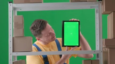 Yeşil arka plan kromatonuna göre çerçevelenmiş. İfade, iş üniforması giyen yetişkin bir erkek. Depodaki bir depocuyu gösteriyor. Kameraya bakan ve gülümseyen bir tablet tutuyor..