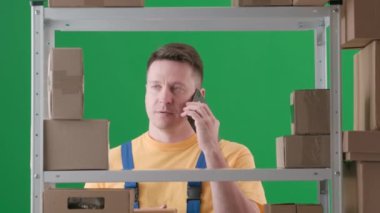 Yeşil arka planda çerçevelenmiş, kromakey. İfade, iş üniforması giyen yetişkin bir erkek. Depodaki bir depocuyu gösteriyor. Telefonda konuşuyor. Sinirli ve huysuz olduğunu söylüyor..