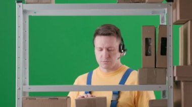 Yeşil arka planda çerçevelenmiş, kromakey. İfade, üniformalı bir adamdır. İfadeler bir depoda depo görevlisi. Kutuları getirdi, rafa koydu ve birileriyle kulaklıkla konuştu..
