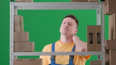 Yeşil renkli arka planda çerçevelenmiş. İş üniformalı yetişkin adam. Depoda bir depocuyu gösteriyor. Mutsuz bir şekilde kollarını ve boynunu yoğuruyor, çalışmaktan yorulmuş, dinlenmek istiyor..