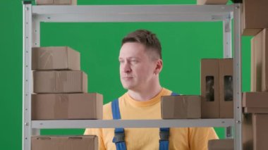 Yeşil arkaplanda, kromakey. İş üniformalı yetişkin adam. Depodaki dükkan sahibini gösteriyor. Elinde bir kutu var ve diğeri de güzel bir jest yapıyor.