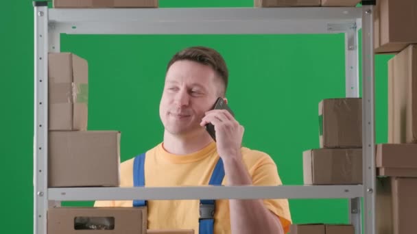 绿色背景相框 铬钥匙 一个穿着工作服的虚构的成年人 描述仓库里的一个店主 他在讲电话 谈论着什么 开心地笑着 — 图库视频影像