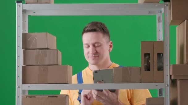 緑色の背景に 染められた 職場の制服を着た大人の男を描く 倉庫に保管庫を設置する 彼はタブレットを保持し 箱をチェックし タブレットに書き込みます — ストック動画
