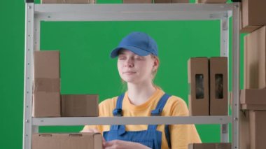 Yeşil arka planda çerçevelenmiş, kromakey. Üniformalı ve şapkalı genç bir kadını gösteriyor. Depoda çalışan bir işçiyi, bir depocuyu gösteriyor. Kutuyu tutuyor, gülümsüyor ve güzel bir jest yapıyor..