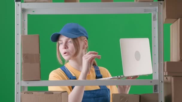緑色の背景にあるフレームでは 染色体 制服を着た若い女性が描かれている 従業員が倉庫に描かれている 彼女はラップトップを持ってチェックし 箱を調べ ノートを取っています — ストック動画