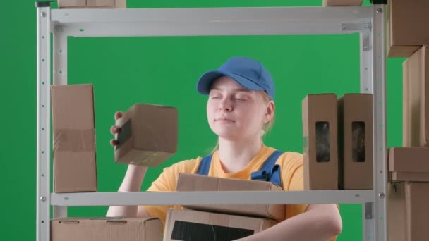 緑色の背景のフレームには スリップがあります 制服を着た若い女性を描く 従業員を倉庫に預ける 彼女は箱のフレームに入り それらを棚に置き 山に置きました — ストック動画