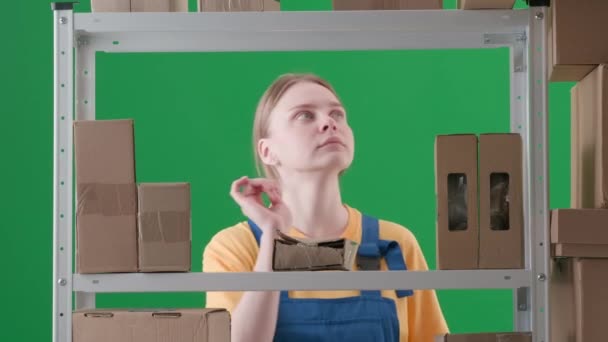 緑色の背景に 染色体を塗りました 制服を着た若い女性を描く 倉庫の保管庫で働く労働者を示しています 彼女は彼女の手に開いた箱を保持し 懐疑的にそれを調べる — ストック動画