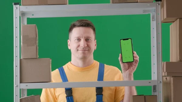 绿色背景相框 铬钥匙 描述是一个穿着工作服的成年男性 演示仓库中的仓库管理员 他拿着手机 面对着摄像机笑了 — 图库照片