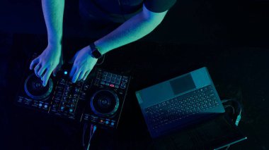 Fotoğraf, bir DJ 'in yetenekli ellerine ses mikserinin düğmelerini ayarlarken, ortam klubünün ışıklandırmasıyla yakınlaşıyor. Kırmızı ellerin canlı kontrastı yeşilin serin tonlarına karşı