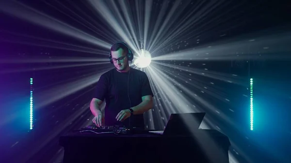 Captivating professional DJ at work in a nightclub setting, with hands on deck controlling sound mixer and turntables. The focused male DJ, wearing headphones, expertly mixes tracks during a live set