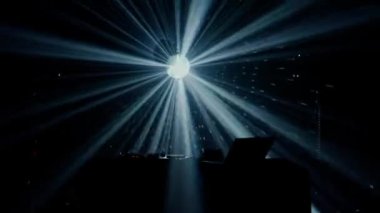 Bu büyüleyici video, canlı bir ışık gösterisinin ortasında, yeşil ve mavi ışık demetleriyle DJ masasının üzerinde dramatik bir etki yaratan bir DJ kurulumu sergiliyor. Kulüp atmosferinin puslu havası