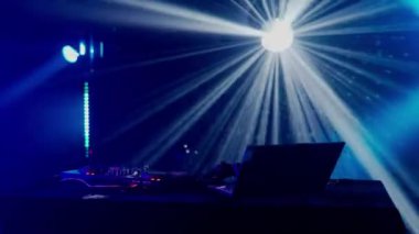 Bu büyüleyici video, canlı bir ışık gösterisinin ortasında, yeşil ve mavi ışık demetleriyle DJ masasının üzerinde dramatik bir etki yaratan bir DJ kurulumu sergiliyor. Kulüp atmosferinin puslu havası