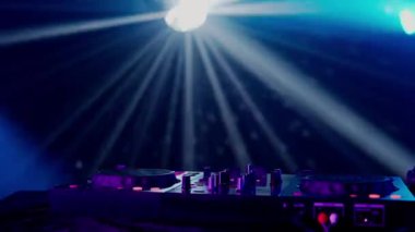 Bu büyüleyici video, canlı bir ışık gösterisinin ortasında, yeşil ve mavi ışık demetleriyle DJ masasının üzerinde dramatik bir etki yaratan bir DJ kurulumu sergiliyor. Kulüp atmosferinin puslu havası