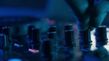 Video, bir DJ 'in becerikli ellerine ses mikserinin düğmelerini ayarlarken, ortam klubünün ışıklandırmasıyla yakınlaşıyor. Kırmızı ellerin canlı kontrastı yeşilin serin tonlarına karşı