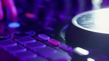 Bu yakın çekim videoda, ses ekipmanlarının karmaşık detaylarını vurgulayan neon lambalarla yıkanmış bir DJ miks tahtası sergileniyor. Pembe ve morlar turntable ve düğmelerde parlıyor
