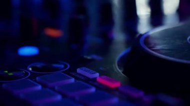 Bu yakın çekim videoda, ses ekipmanlarının karmaşık detaylarını vurgulayan neon lambalarla yıkanmış bir DJ miks tahtası sergileniyor. Pembe ve morlar turntable ve düğmelerde parlıyor