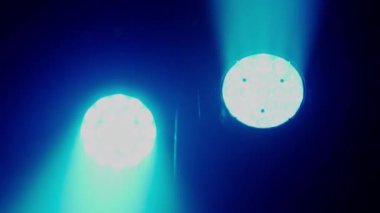 Videoda bir gece kulübünün karanlığını kesen bir çift yoğun mavi sahne ışığı görülüyor. Güçlü ışınlar dramatik ve karamsar bir atmosfer yaratıyor. Canlı müzik mekanı ya da dans için tipik bir ortam.