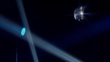 Video, ön planda, çevre ışıklarının hafifçe aydınlattığı klasik bir disko topunu net bir şekilde yakalıyor. Sağda, koyu mavi bir renkle yıkanmış bir sahne ışığı retro diskoya modern bir kıvrım katıyor.