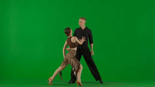 优雅的交际舞双人在生动的绿色背景下表演动态的舞步 这位男舞蹈家穿着华丽的黑色服装 一只手摆出一种姿势 — 图库照片