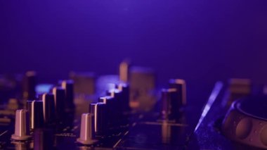 Bu yakın çekim videoda, ses ekipmanlarının karmaşık detaylarını vurgulayan neon lambalarla yıkanmış bir DJ miks tahtası sergileniyor. Pembe ve morlar turntable ve düğmelerde parlıyor