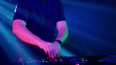 Video, bir DJ 'in becerikli ellerine ses mikserinin düğmelerini ayarlarken, ortam klubünün ışıklandırmasıyla yakınlaşıyor. Kırmızı ellerin canlı kontrastı yeşilin serin tonlarına karşı