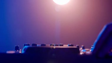 Video, bir DJ 'in becerikli ellerine ses mikserinin düğmelerini ayarlarken, ortam klubünün ışıklandırmasıyla yakınlaşıyor. Kırmızı ellerin canlı kontrastı yeşilin serin tonlarına karşı