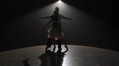 Spotlight 'taki zarif balo dansçısı çift. Bu çarpıcı video, performanslarının ortasında, karanlığa karşı tek bir spot ışığı altında dans eden bir çiftin görüntülerini yakalıyor.