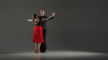 Spotlight 'taki zarif balo dansçısı çift. Bu çarpıcı görüntü, gösterinin ortasında, karanlığa karşı tek bir spot ışığıyla çevrili, dans eden bir çiftin görüntüsünü yakalıyor.