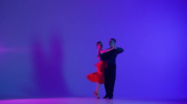 Spotlight 'taki zarif balo dansçısı çift. Bu çarpıcı görüntü, gösterinin ortasında, karanlığa karşı tek bir spot ışığıyla çevrili, dans eden bir çiftin görüntüsünü yakalıyor.