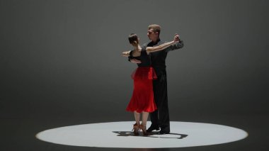 Spotlight 'taki zarif balo dansçısı çift. Bu çarpıcı görüntü, gösterinin ortasında, karanlığa karşı tek bir spot ışığıyla çevrili, dans eden bir çiftin görüntüsünü yakalıyor.