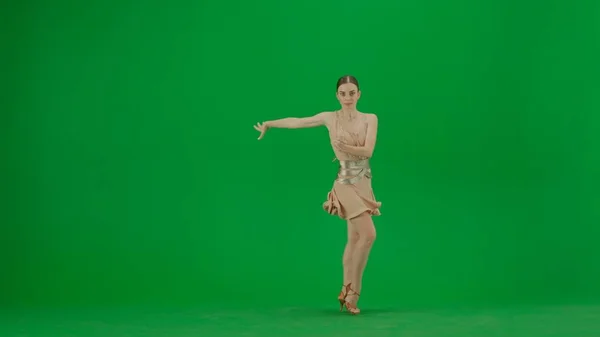 Latin Ballroom Dancer in Pose Against Green Screen. A poised Latin ballroom dancer stands against a green screen backdrop, her form exuding elegance and control. Clad in a beige dance dress with