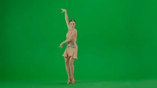 Latin Ballroom Dancer in Pose Against Green Screen. A poised Latin ballroom dancer stands against a green screen backdrop, her form exuding elegance and control. Clad in a beige dance dress with