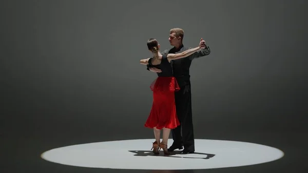 Elegant Ballroom Dance Couple on Spotlight. This striking image captures a ballroom dancing couple mid-performance, enveloped in a singular spotlight against the darkness, highlighting their form and